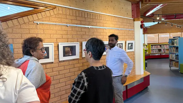 Visitors look at framed photographs and talk with a man in a white shirt.