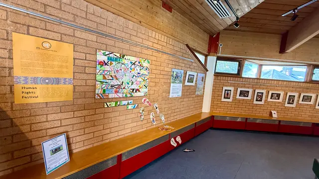 A colourful collage artwork and an information panel on the brick wall of the gallery.