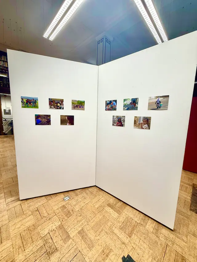 Two white display walls in a library, hung with small colour photographs.