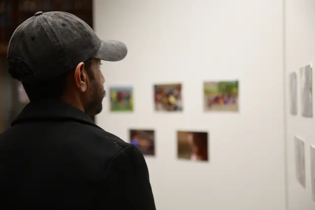 Seen from behind, a visitor in a cap looks at photographs on a display wall.