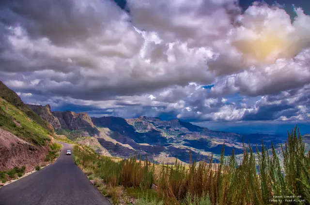 A road winds through a mountain pass beneath dramatic clouds.