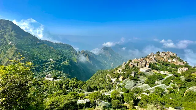 Terraced green mountains under a blue sky, with a village along the ridge.