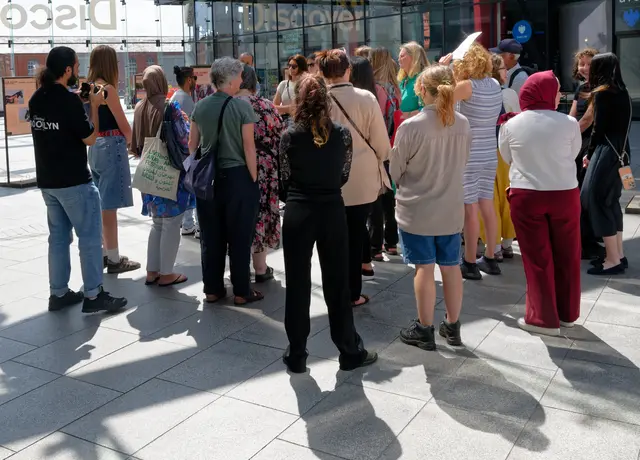 A crowd gathers in the sunlit atrium around the exhibition panels.
