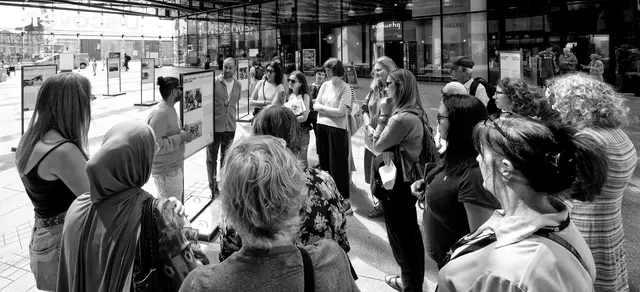 Black-and-white view of visitors gathered around the exhibition panels in the atrium.